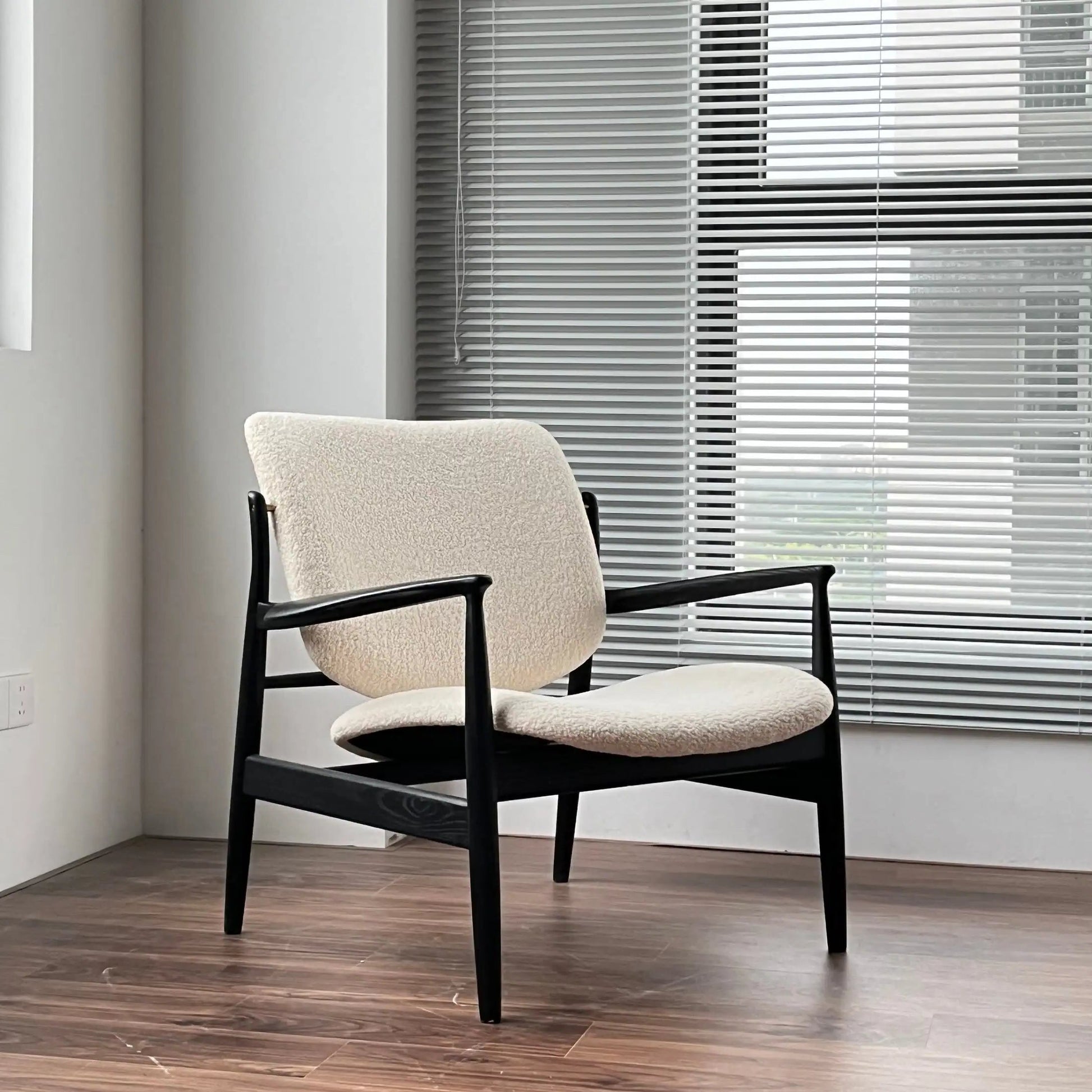 Beige armchair with black frame in a room with wooden flooring and window blinds.